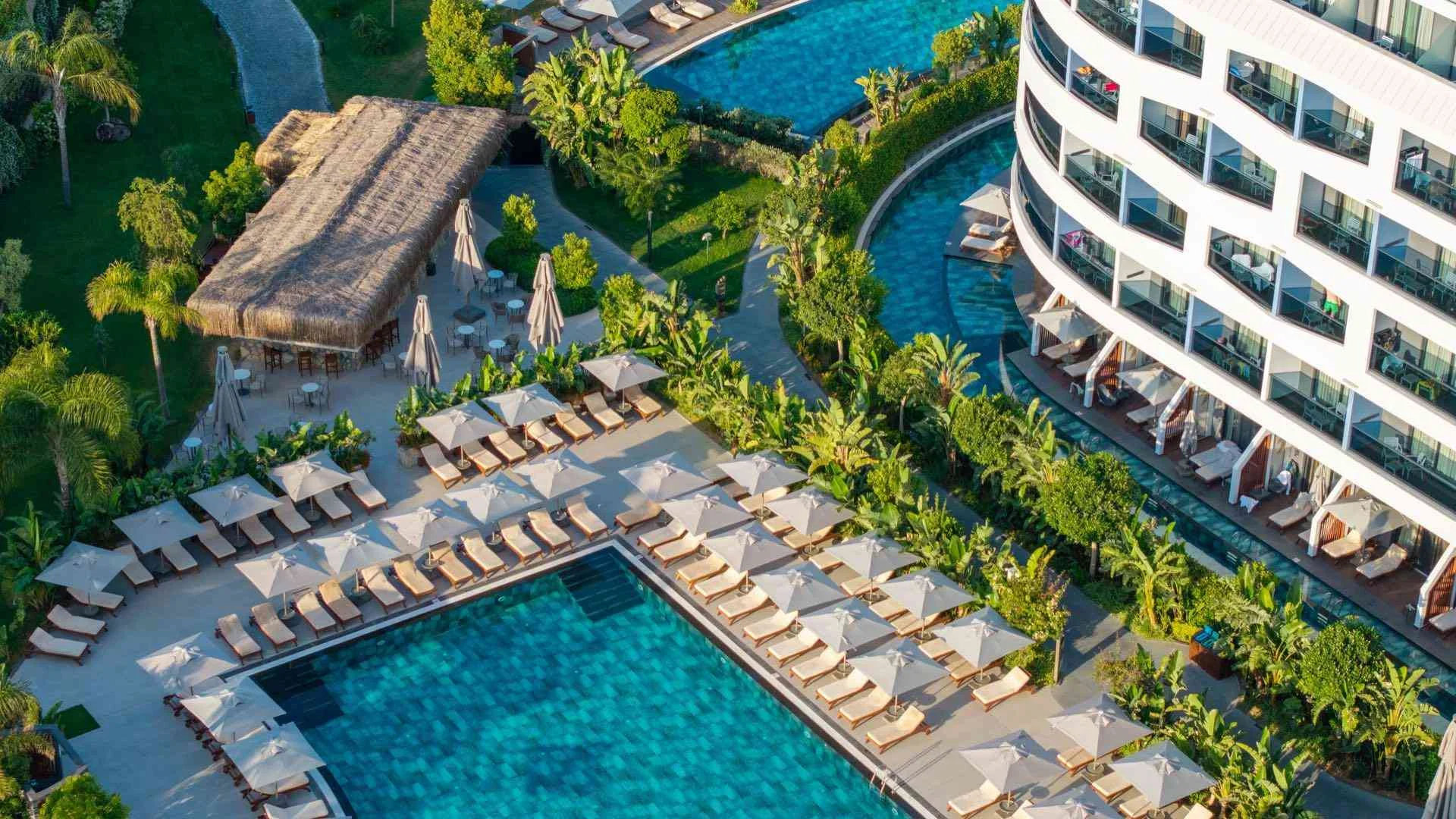LIU Resorts · Moderner Hotelpool umgeben von Liegestühlen und üppiger Vegetation neben einem runden Gebäude.